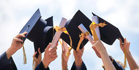 Graduates in blue gowns raise caps and diplomas against a clear sky, symbolizing achievement and new beginnings, reflecting the Christopher Smith Foundation’s commitment to caregiver recognition and support within the disability community.| A Non Profit For Caregivers | Christopher Smith Foundation