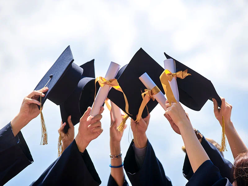 Graduates in blue gowns raise caps and diplomas against a clear sky, symbolizing achievement and new beginnings, reflecting the Christopher Smith Foundation’s commitment to caregiver recognition and support within the disability community.| A Non Profit For Caregivers | Christopher Smith Foundation