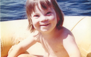 A joyful child with light brown hair smiles while sitting in a yellow inflatable boat on a lake, representing the spirit of the Christopher Smith Foundation's caregiver support for the disability community.| A Non Profit For Caregivers | Christopher Smith Foundation