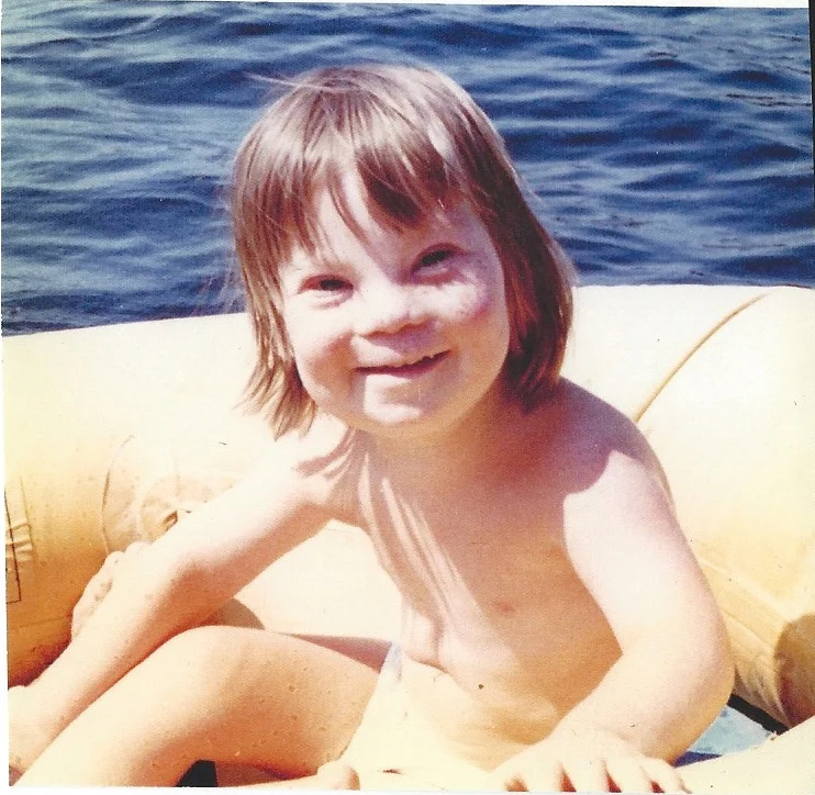 A joyful child with light brown hair smiles while sitting in a yellow inflatable boat on a lake, representing the spirit of the Christopher Smith Foundation's caregiver support for the disability community.| A Non Profit For Caregivers | Christopher Smith Foundation