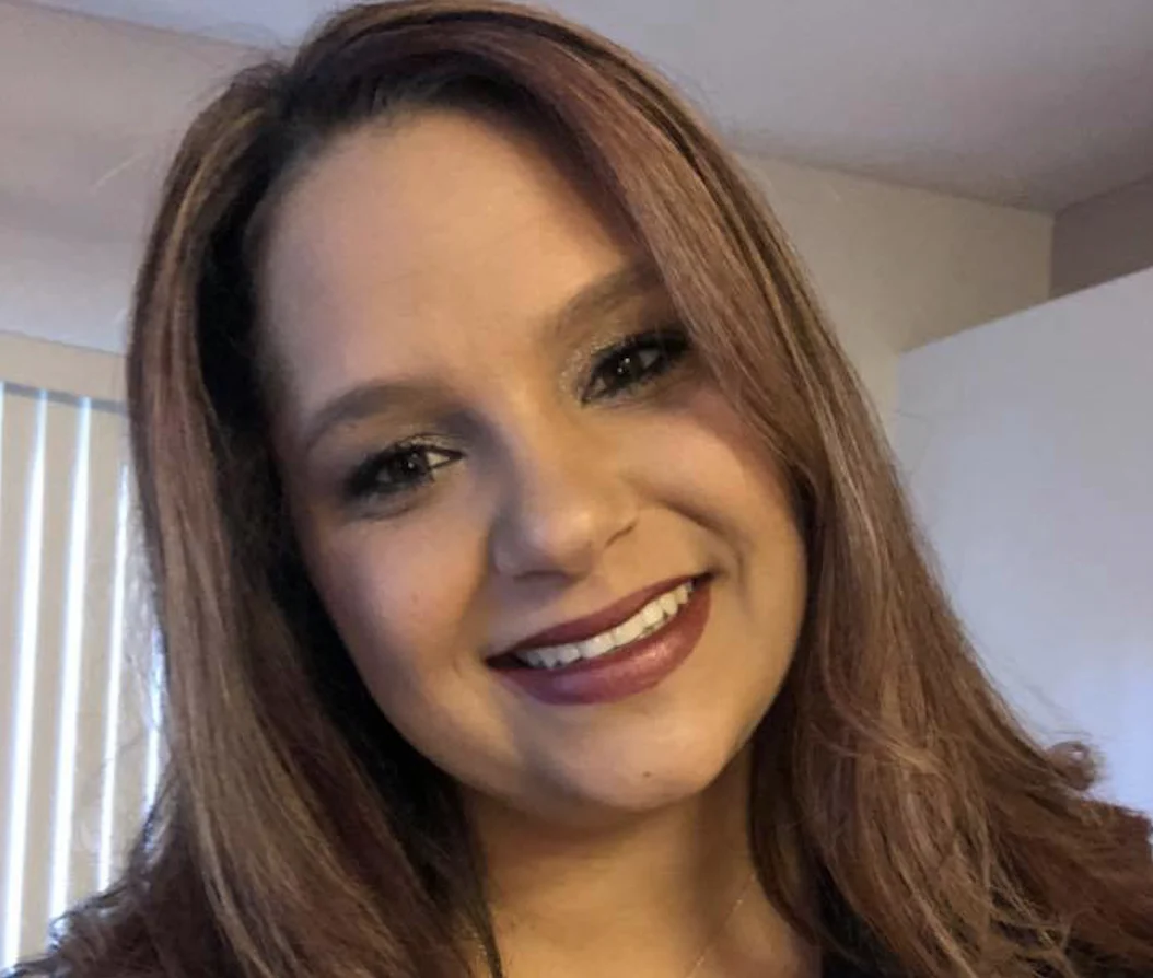 A smiling woman with long hair stands indoors, embodying the spirit of caregiver support promoted by the Christopher Smith Foundation, which honors caregivers of people with disabilities.| A Non Profit For Caregivers | Christopher Smith Foundation