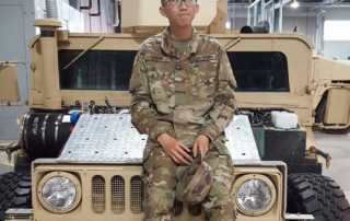 A person in military uniform sits on a vehicle, holding a hat indoors. The Christopher Smith Foundation supports caregivers of people with disabilities, emphasizing community and recognition.| A Non Profit For Caregivers | Christopher Smith Foundation