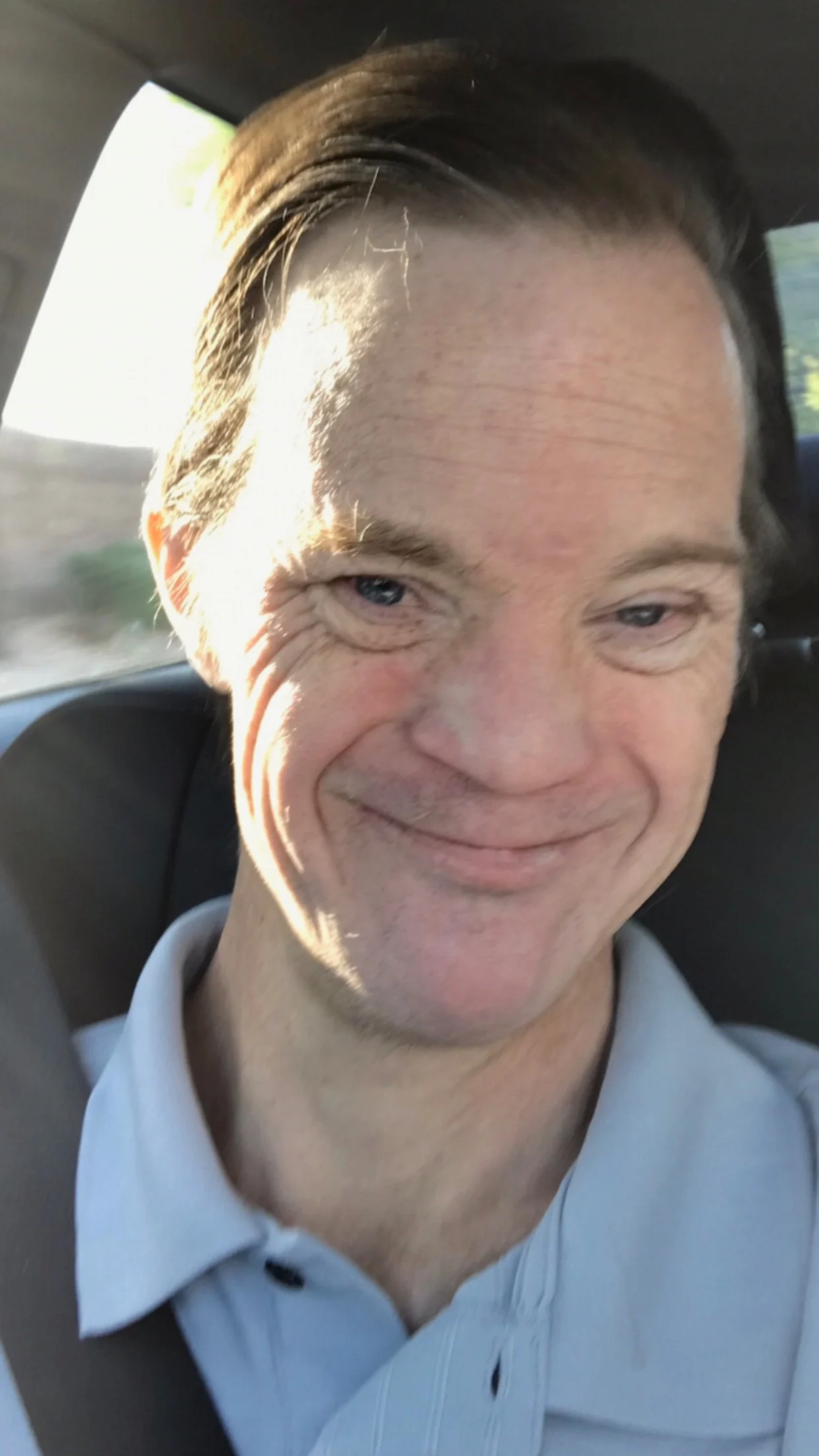 A man with light skin and short hair smiles warmly while seated in a car, wearing a light blue polo shirt. The image reflects the Christopher Smith Foundation's mission of caregiver support and disability advocacy.| A Non Profit For Caregivers | Christopher Smith Foundation