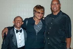 Three smiling people, standing arm in arm, with one in a tuxedo, embodying the spirit of the Christopher Smith Foundation's mission in caregiver support and disability advocacy, set against a plain background, highlighting unity and compassion.| A Non Profit For Caregivers | Christopher Smith Foundation