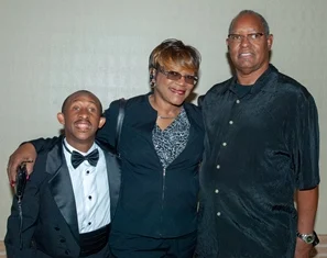 Three smiling people, standing arm in arm, with one in a tuxedo, embodying the spirit of the Christopher Smith Foundation's mission in caregiver support and disability advocacy, set against a plain background, highlighting unity and compassion.| A Non Profit For Caregivers | Christopher Smith Foundation