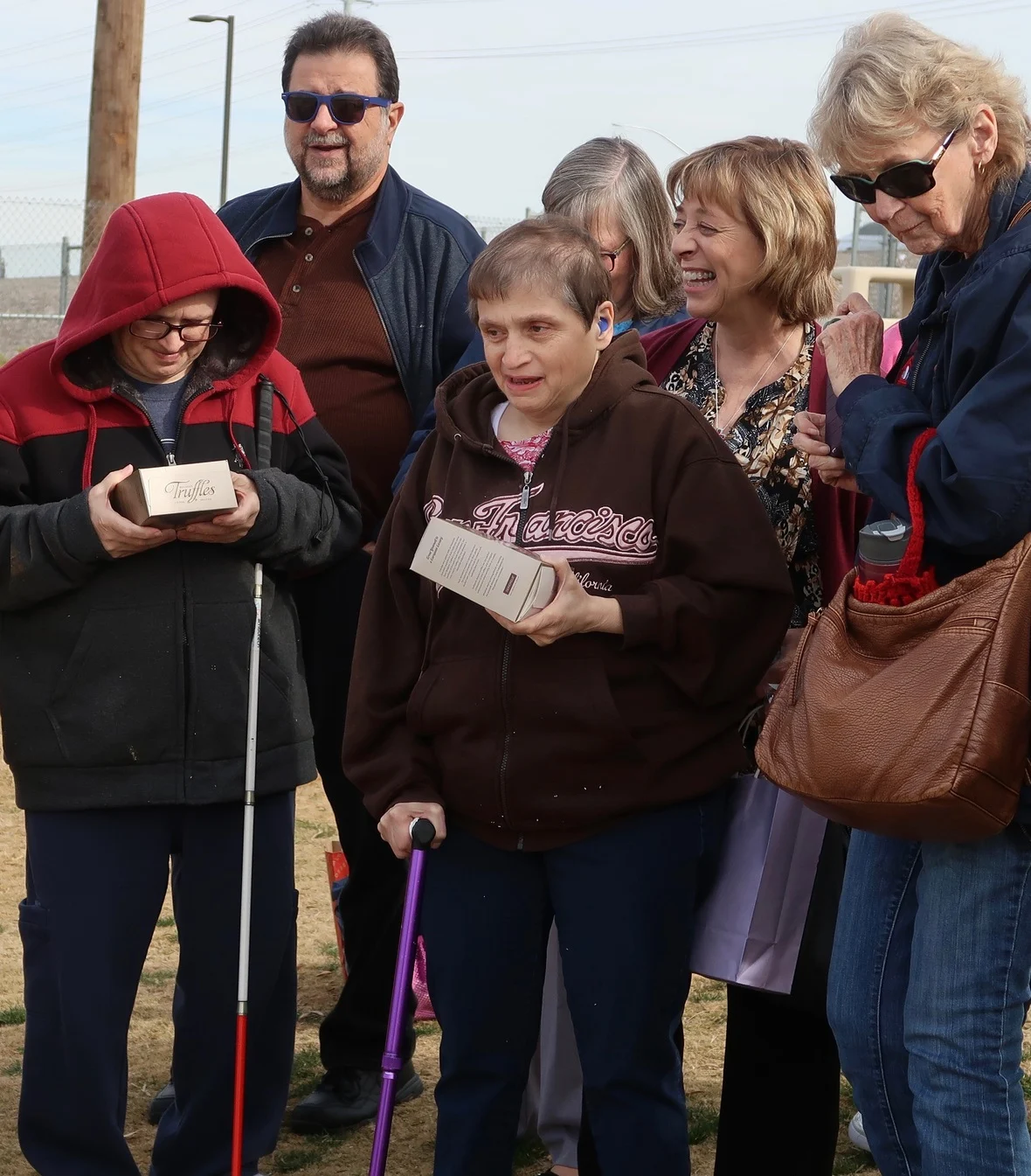 A group of smiling people, some holding boxes of truffles, gather outdoors, highlighting joy and community. This reflects the Christopher Smith Foundation's mission of caregiver support and recognition within the disability community.| A Non Profit For Caregivers | Christopher Smith Foundation