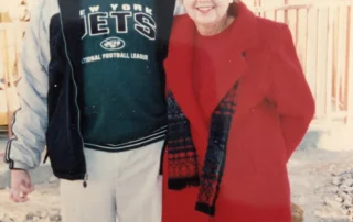 A smiling man in a New York Jets shirt and woman in a red coat stand together outdoors, embodying caregiver support and community spirit, reflecting the mission of the Christopher Smith Foundation in disability advocacy and family caregivers.| A Non Profit For Caregivers | Christopher Smith Foundation