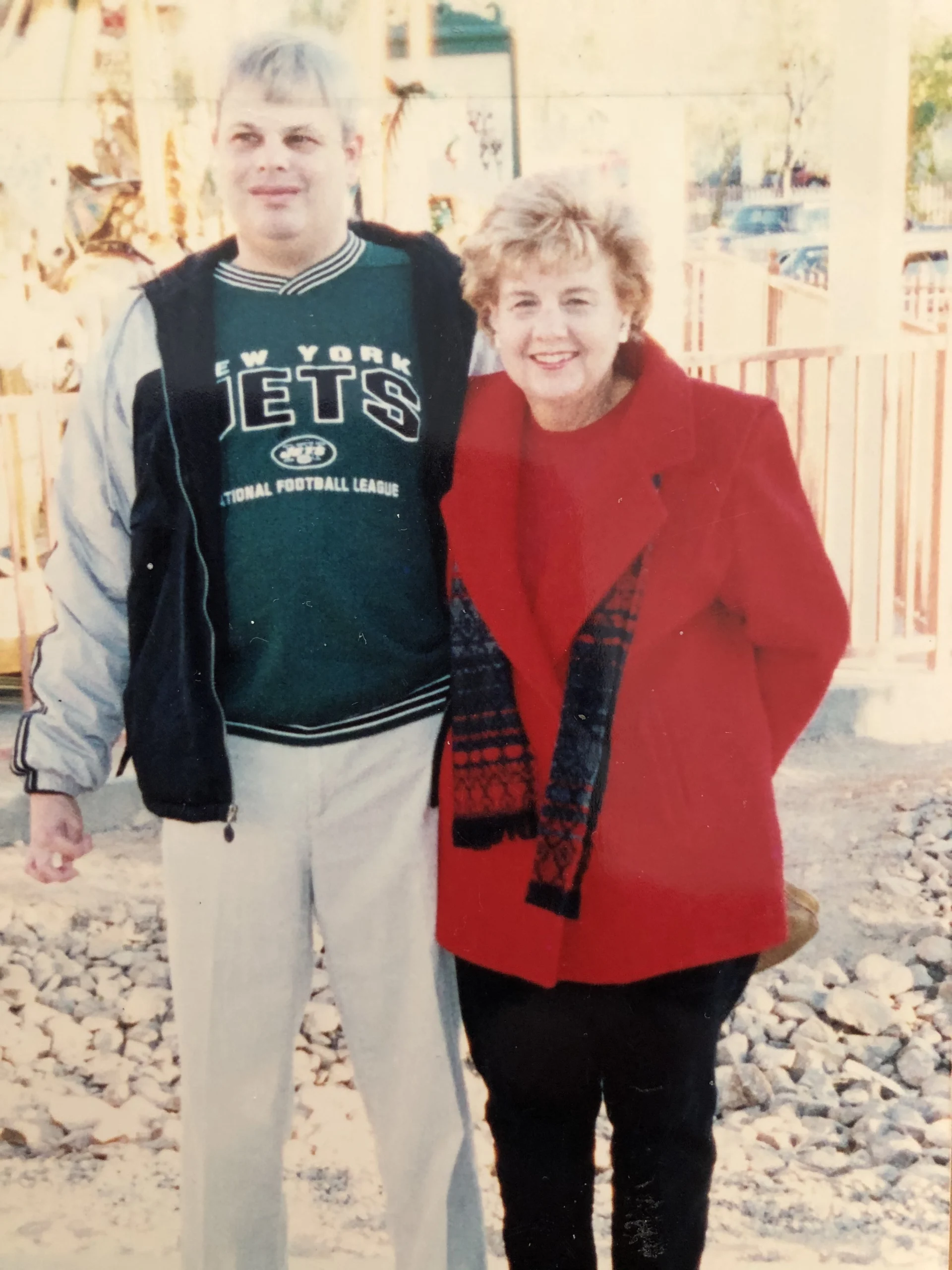 A smiling man in a New York Jets shirt and woman in a red coat stand together outdoors, embodying caregiver support and community spirit, reflecting the mission of the Christopher Smith Foundation in disability advocacy and family caregivers.| A Non Profit For Caregivers | Christopher Smith Foundation