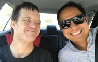 A man wearing sunglasses smiles warmly at another man in a car. They share a joyful moment, highlighting caregiver support within the disability community, reflecting the mission of the Christopher Smith Foundation.| A Non Profit For Caregivers | Christopher Smith Foundation