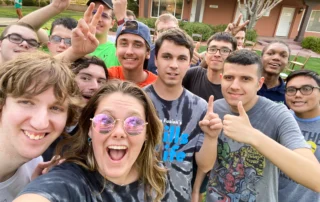 A group of young people, some wearing glasses and colorful t-shirts, smile and make peace signs outdoors, embodying joy and community. This image highlights the essence of caregiver support and disability advocacy by the Christopher Smith Foundation.| A Non Profit For Caregivers | Christopher Smith Foundation