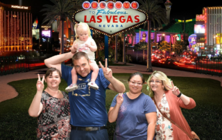 A group of five people, including a child on a man's shoulders, pose happily in front of the illuminated Las Vegas sign. This image reflects…| A Non Profit For Caregivers | Christopher Smith Foundation