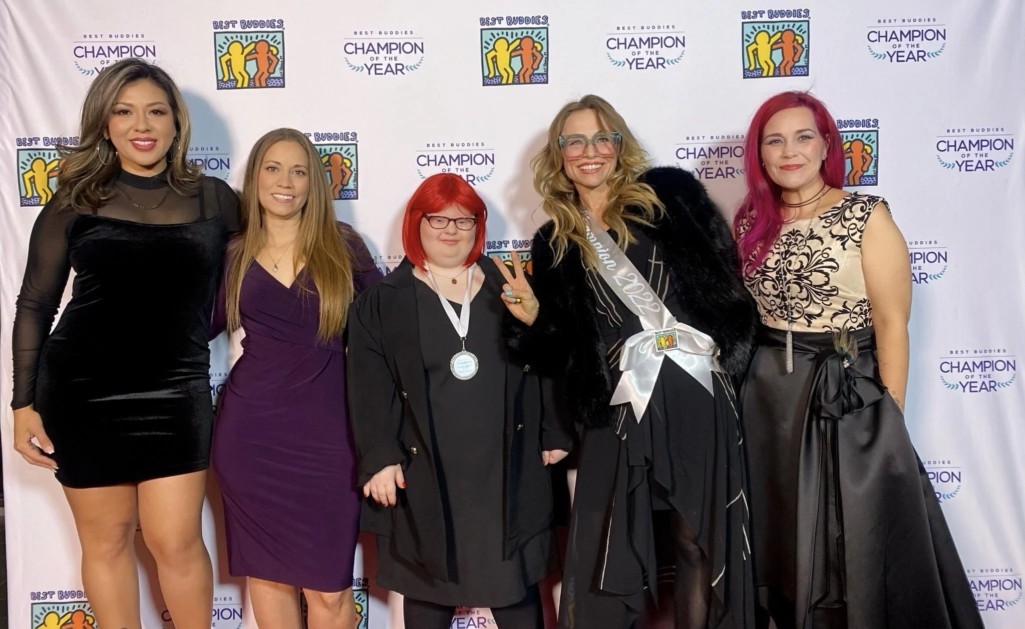 Five women stand smiling in elegant dresses at a Christopher Smith Foundation event, celebrating caregiver recognition. The backdrop features logos and the phrase "Champion of the Year," highlighting support for the disability community.| A Non Profit For Caregivers | Christopher Smith Foundation