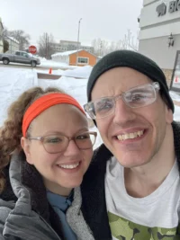 A smiling pair in winter attire poses outside with snow and buildings in the background, embodying the spirit of the Christopher Smith Foundation’s commitment to caregiver recognition and support for the disability community.| A Non Profit For Caregivers | Christopher Smith Foundation