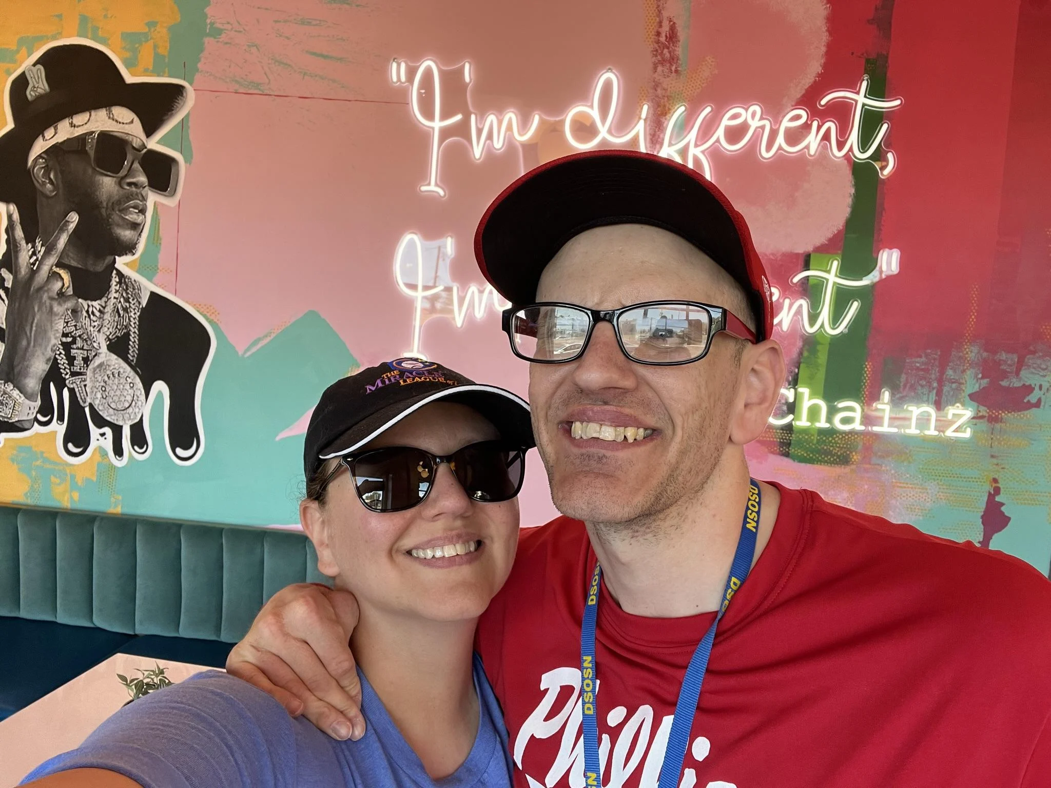 A smiling couple in casual attire poses in front of a colorful mural. The Christopher Smith Foundation supports caregivers of people with disabilities, highlighting moments of joy and connection in the disability community.| A Non Profit For Caregivers | Christopher Smith Foundation