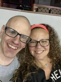 A smiling man and woman, both wearing glasses, pose closely together. The Christopher Smith Foundation supports caregivers of people with disabilities, recognizing their vital role.| A Non Profit For Caregivers | Christopher Smith Foundation