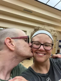 A man kisses a smiling woman on the cheek in a warmly lit room, illustrating the bond between caregivers of people with disabilities and their loved ones, reflecting the Christopher Smith Foundation's mission of caregiver support and recognition.| A Non Profit For Caregivers | Christopher Smith Foundation