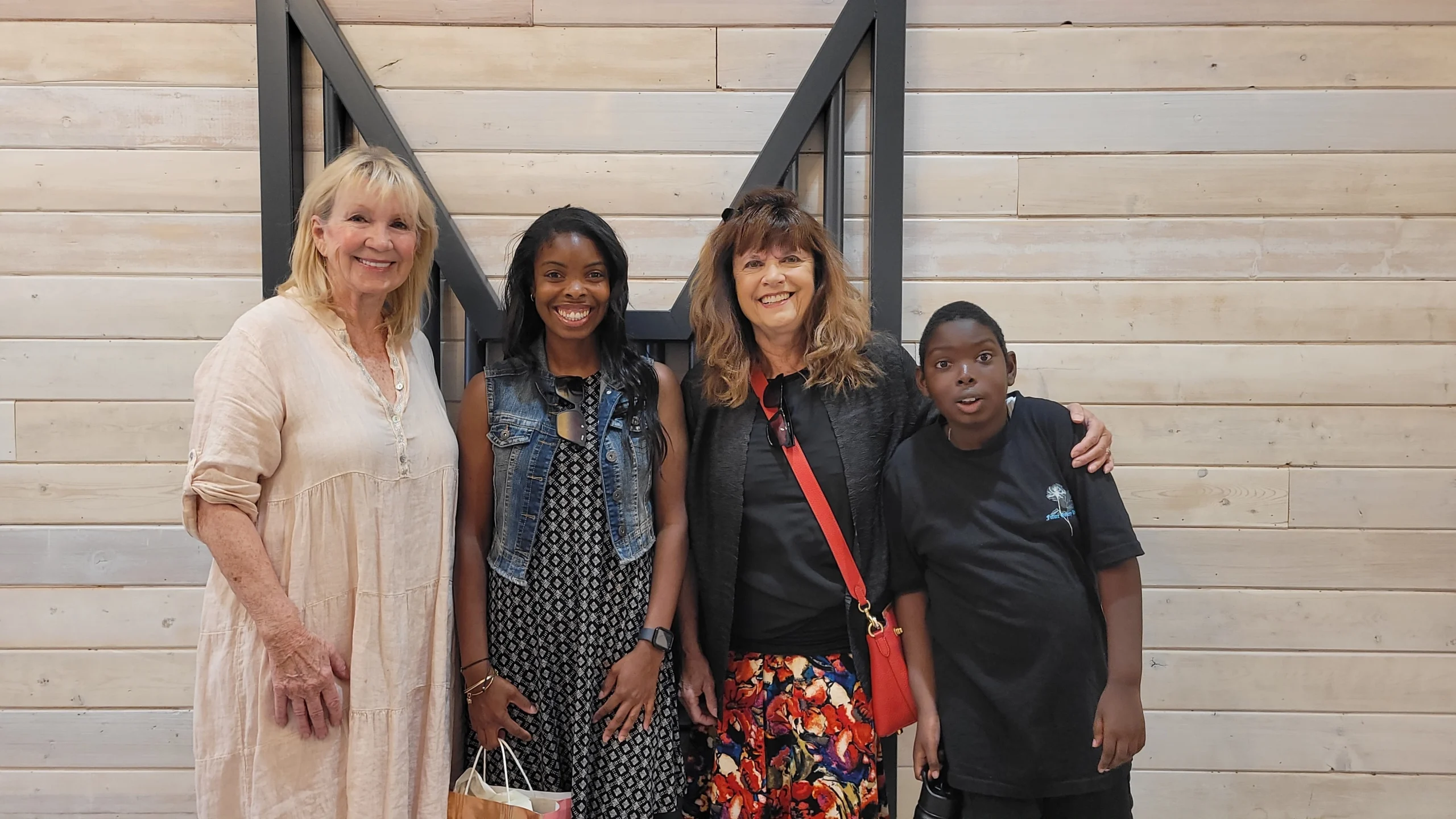 Four smiling people stand together in front of a light wooden wall, embodying the spirit of caregiver support celebrated by the Christopher Smith Foundation.| A Non Profit For Caregivers | Christopher Smith Foundation