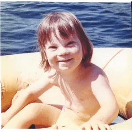 A young child with a joyful smile sits in a yellow inflatable boat on a lake. The image represents the Christopher Smith Foundation’s mission of…| A Non Profit For Caregivers | Christopher Smith Foundation